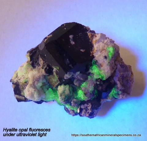 Hyalite opal and feldspar sit on a group of schorl crystals